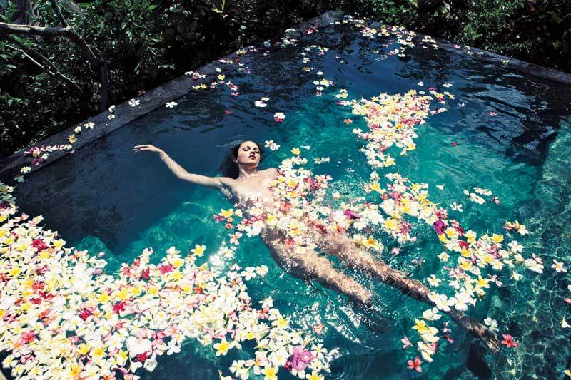 Прекрасная балийка с цветком в волосах обнаженная в саду у бассейна