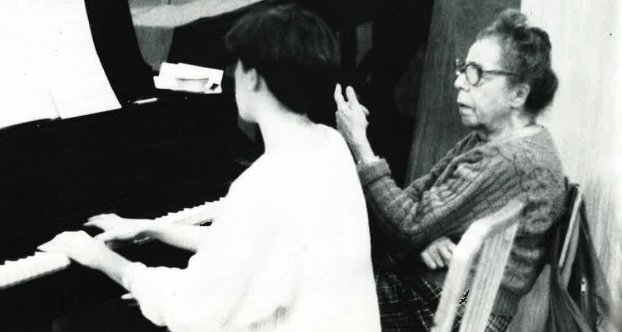 Piano teacher Bertha Bush guides a student at the piano.