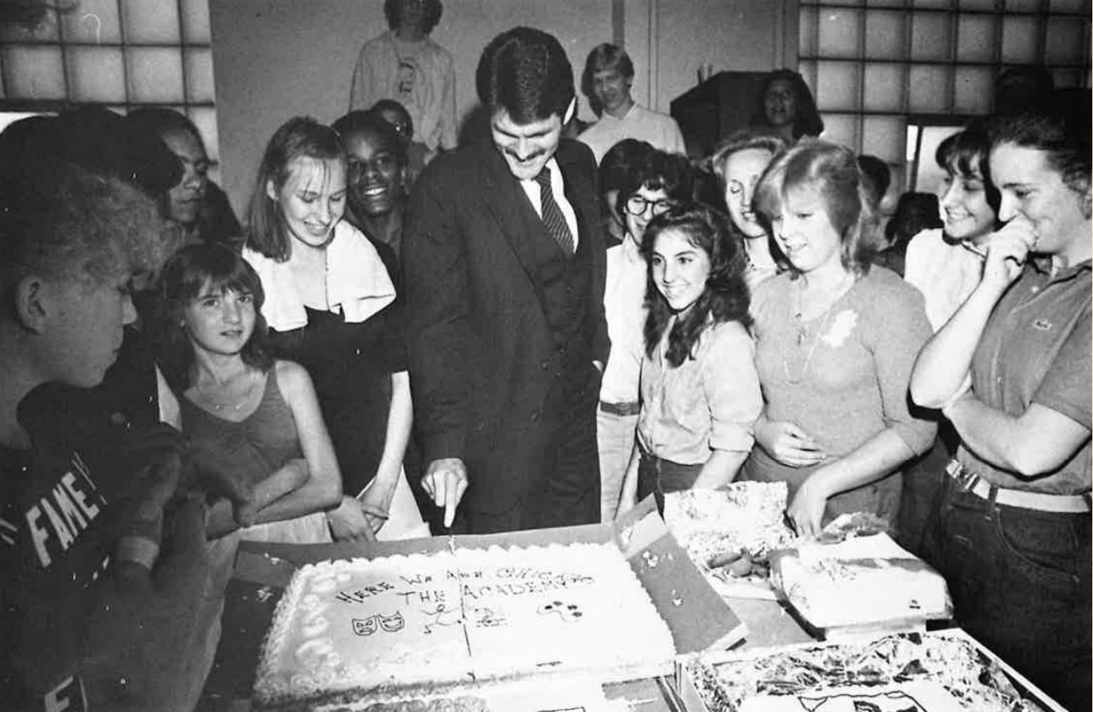 Larry Jordan cuts into a cake on the first day of school at The Academy, surrounded by excited students.