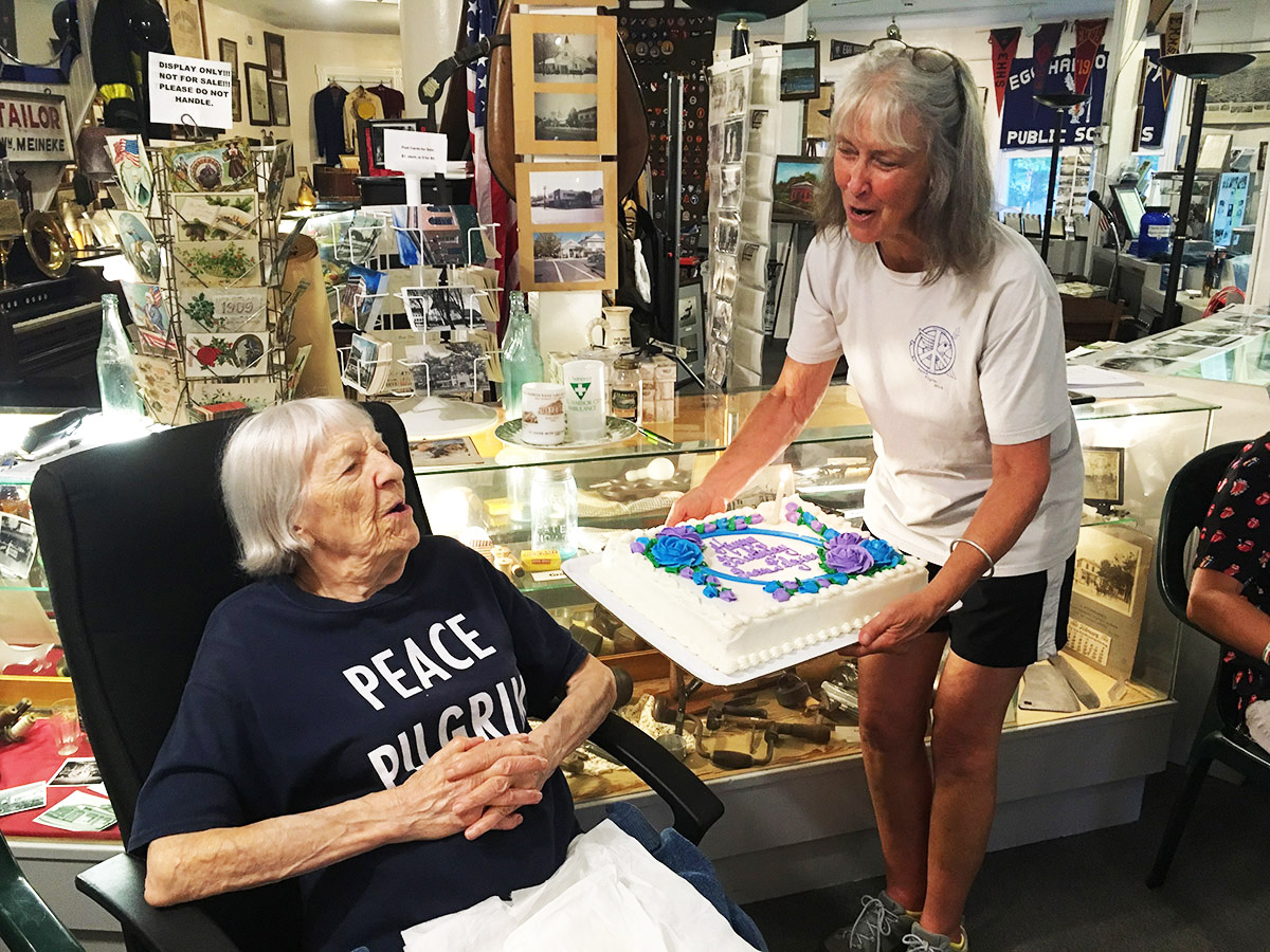 Peace Pilgrim's sister, Helene Young (age 104) gets ready to blow out the candle on the birthday cake held by FoPP board member Barbara Reynolds