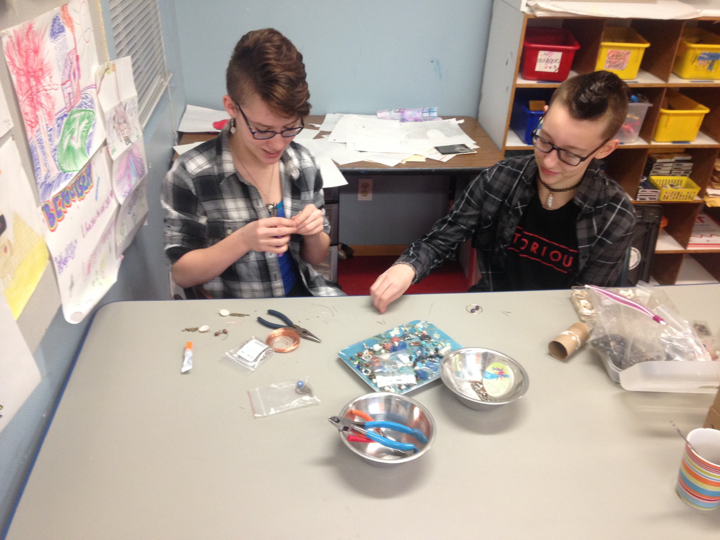两个学生在一张桌子上用各种各样的手工用品做手工.