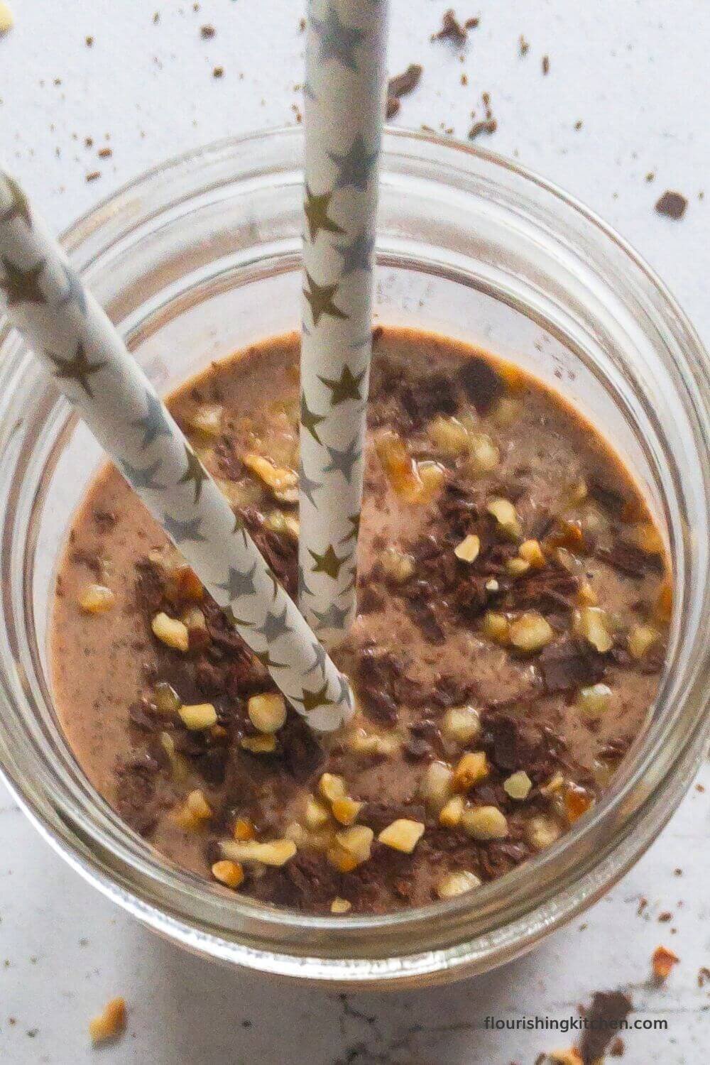 奶昔的顶部俯视着切碎的榛子和磨碎的巧克力的浇头。用金色和银色星星的2个吸管伸出罐子的顶部。