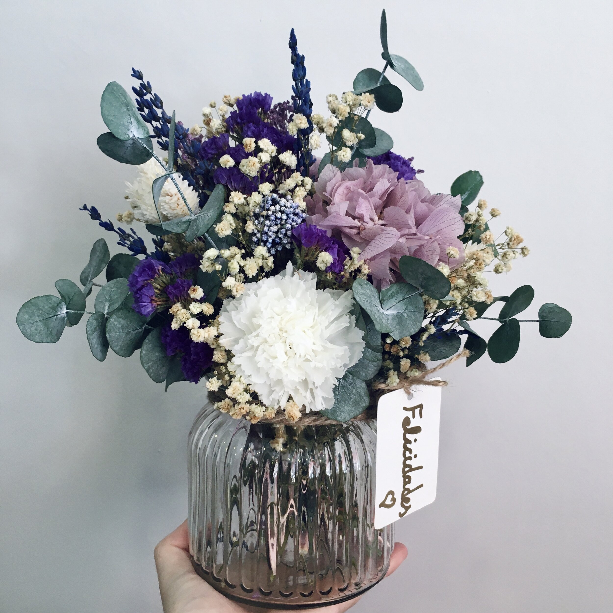 Jarrón de cristal con flores preservadas con hortensias y paniculata.