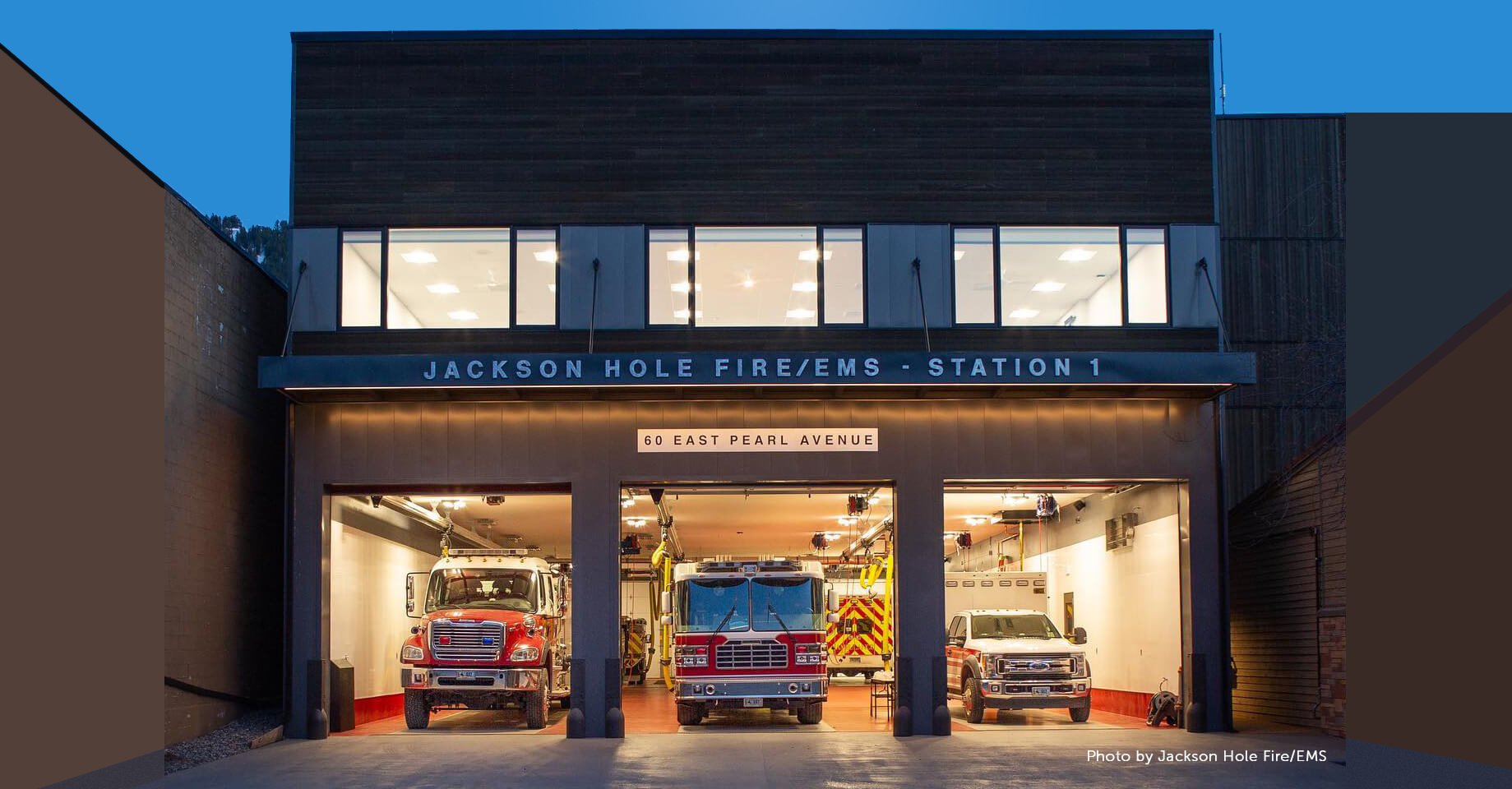 Three emergency vehicles in opened doors of a fire station at twilight