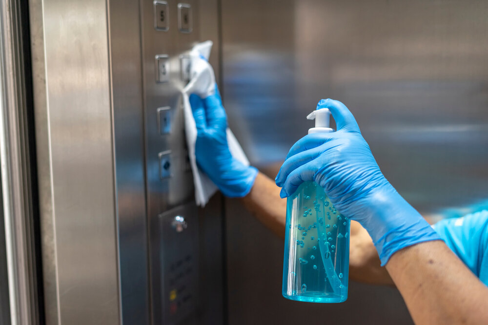 特写老员工的手使用湿擦清洁电梯按钮控制面板与蓝色的消毒瓶.消毒、清洁和保健、抗冠状病毒、COVID-19.有选择性的重点