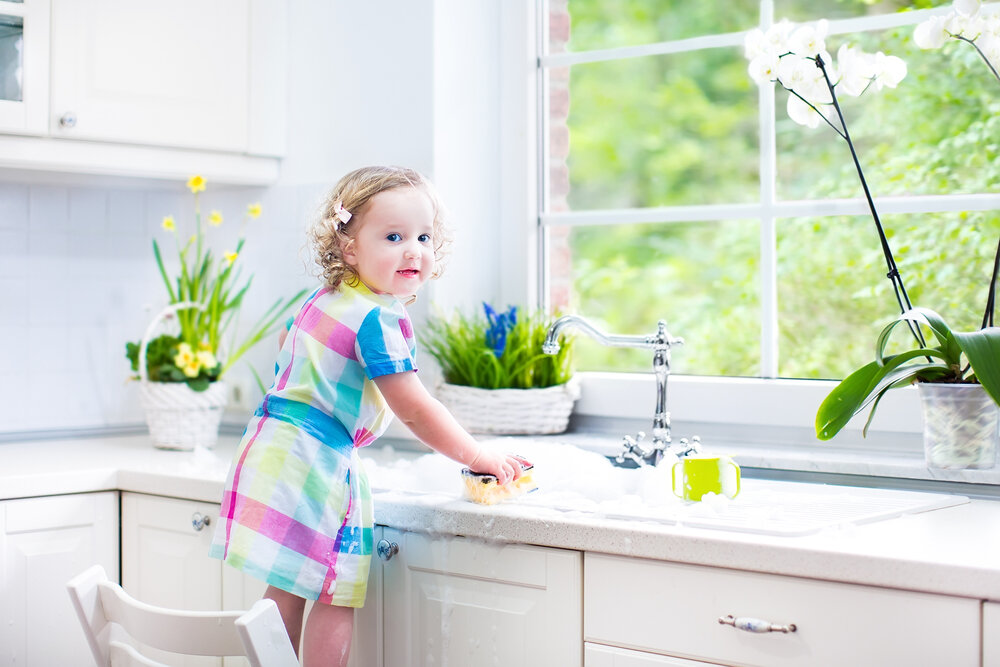 可爱的卷发小女孩穿着五颜六色的裙子洗碗, 在一个美丽的阳光明媚的白色厨房里，在一个现代的家庭里，用海绵清洁，在水池里玩泡沫.jpg