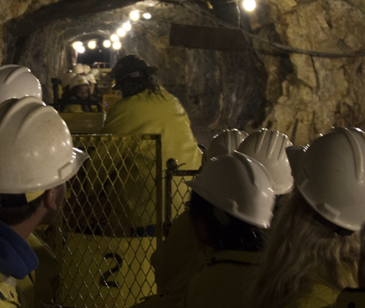 People in rain jackets and helmets on a mine cart going into a cave