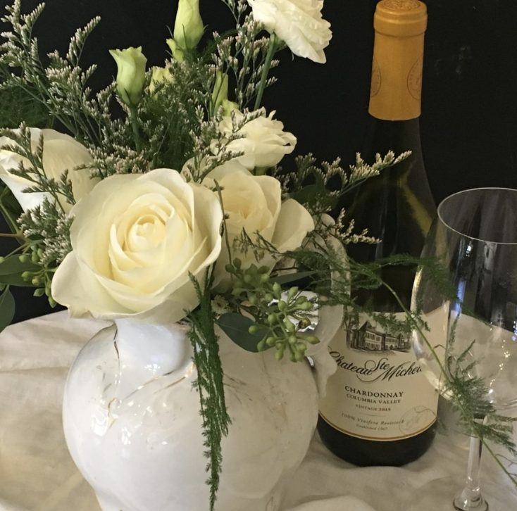 White vase with white flowers, bottle of wine and wine glass