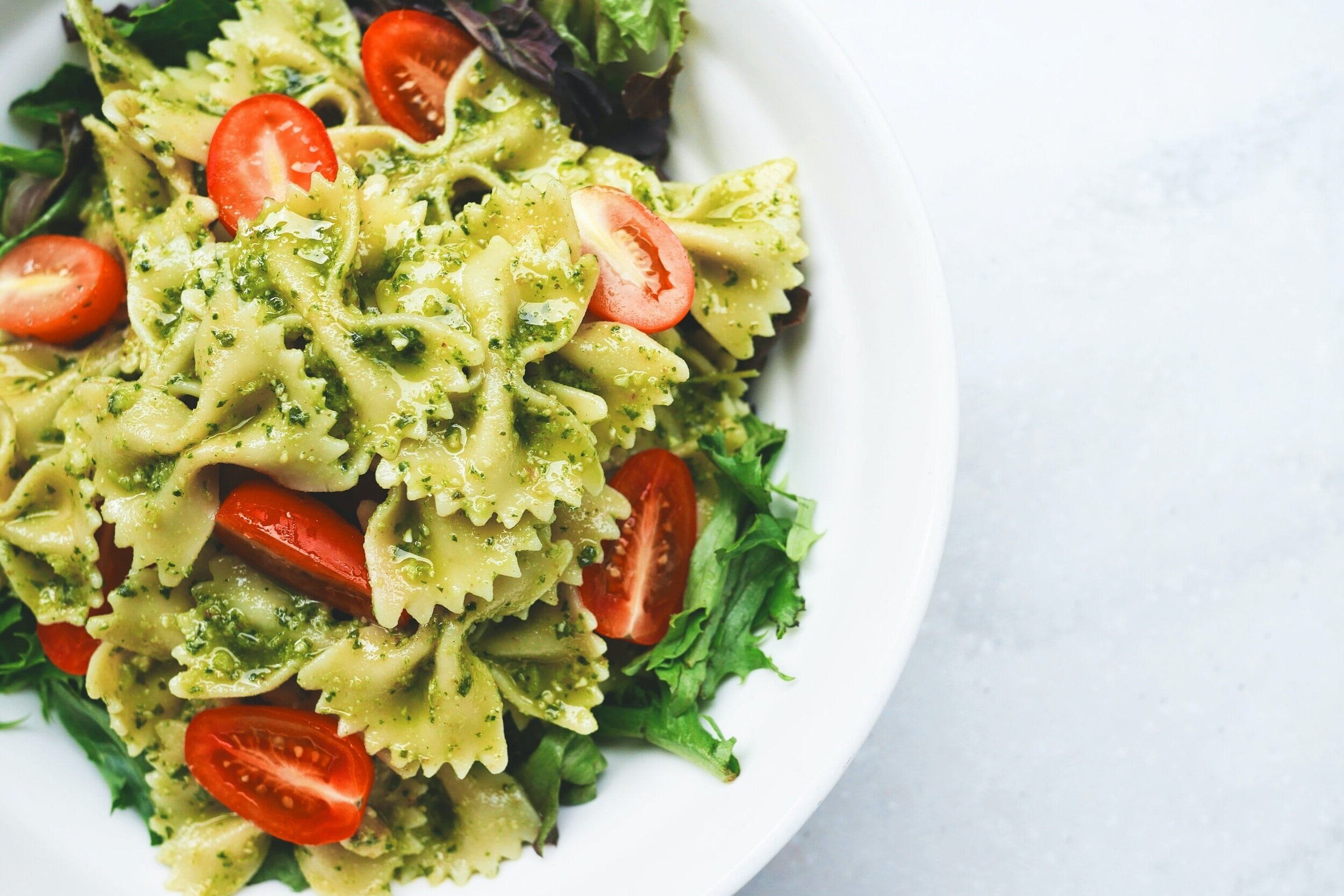 pesto pasta with tomatoes and lettuce on white plate