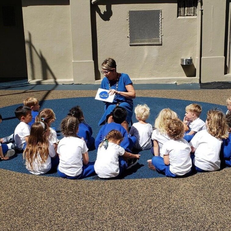 孩子们围成一圈坐着，一个女人给他们读故事