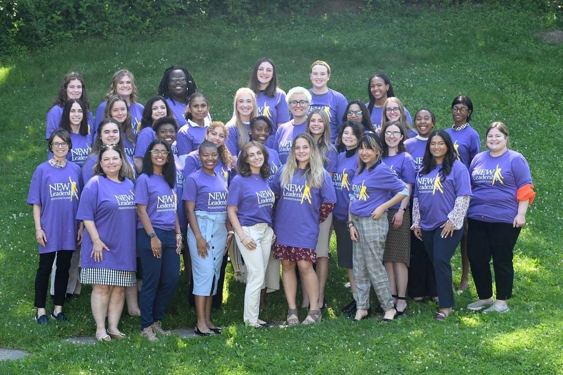 照片中的一群女人都穿着同样的紫色NEW Leadership t恤, 在外面摆姿势拍照