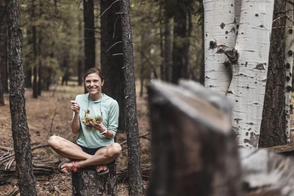 girl eating while sitting on top of a tree stump smiling at the camera