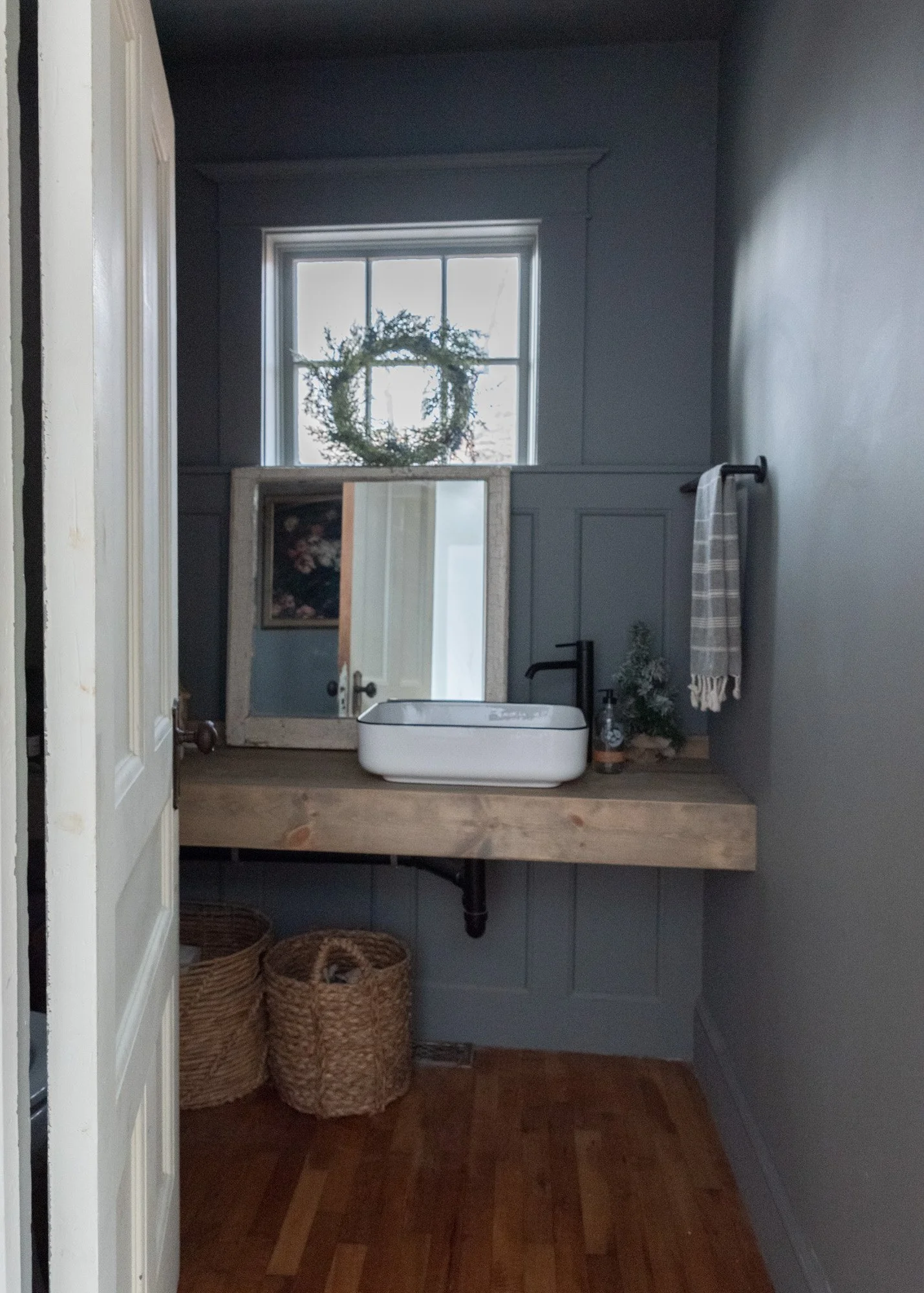 The Wild decoelis | 2020 Holiday Home Tour | Dark gray powder room with wood floating vanity vessel sink black tap vintage mirror and baskets Hardwood floors
