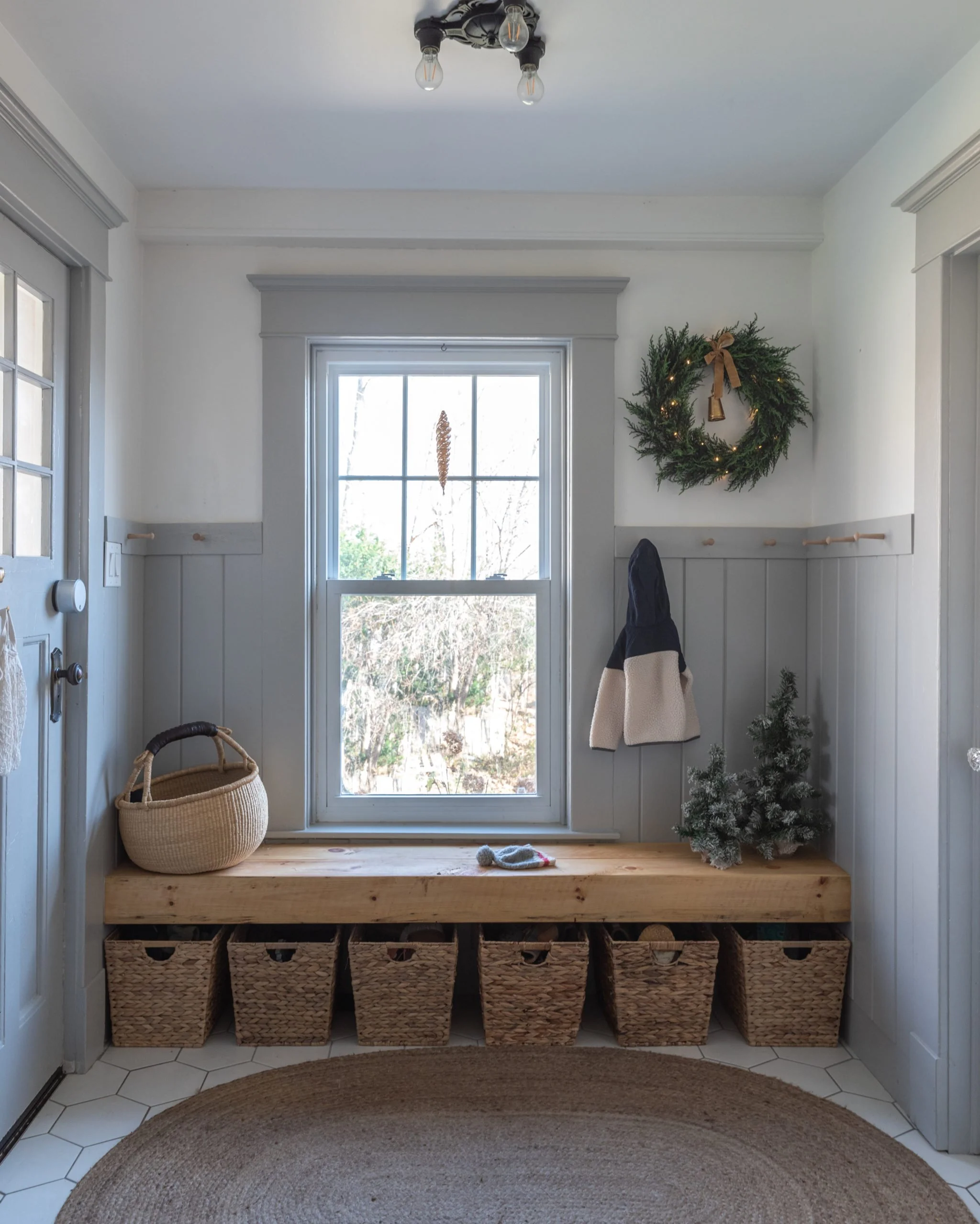 The Wild decoelis | 2020 Holiday Home Tour | Mud room with gray wainscotting and shaker peg rail, floating wood bench, baskets for shoes, mini trees and cedar wreath, traditional farmhouse