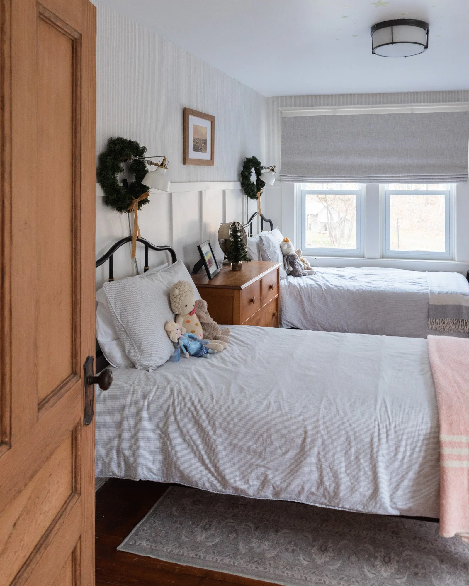 The Wild Decoelis | Holiday Home Tour | Kids room holiday decor with two twin beds, wreaths over sconces, gray pinstripe wallpaper, white board and batten, gray striped betting