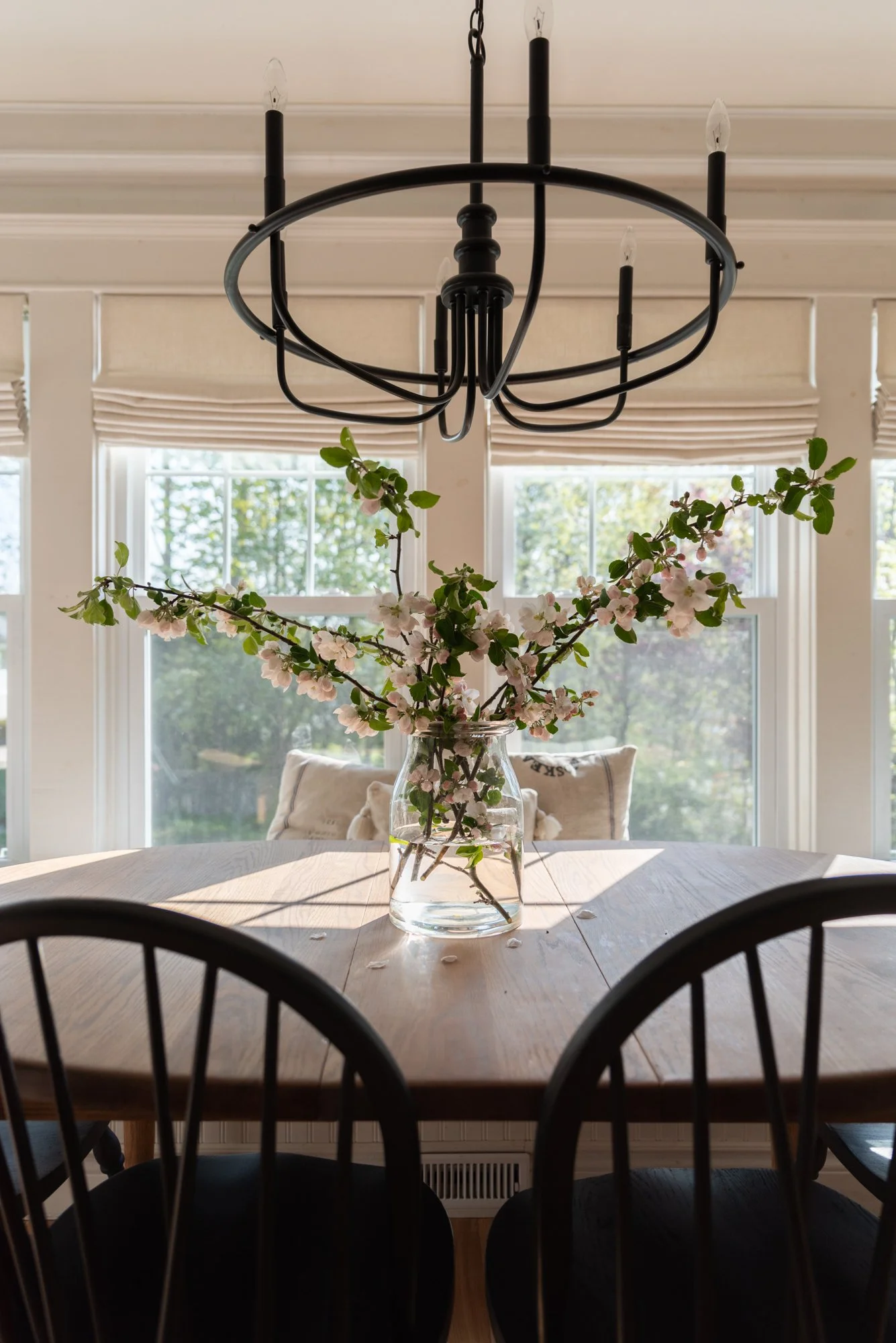 the wild decoelis | apple blossom branches in the house as decorations. Built in bench, refinished wood floors, black chairs, baskers, black vase, black chandelier, vintage art.