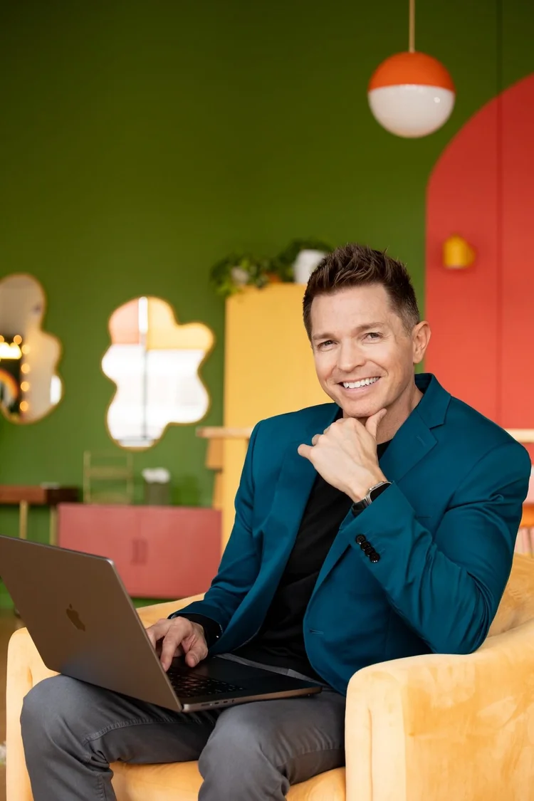Photo of Tony Vincent sitting in a chair looking at the camera with a computer on his lap