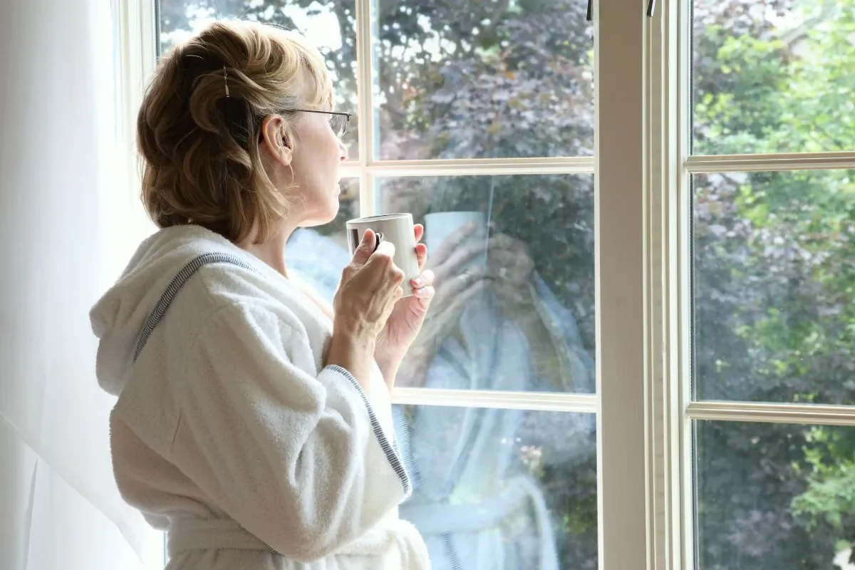 Woman looking out a window with a cup of coffee, taking a reflective moment to think about her relationship