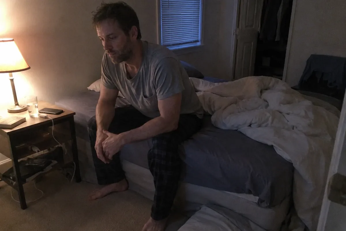 A person sitting on the edge of a bed unable to sleep in the days after discovering an affair