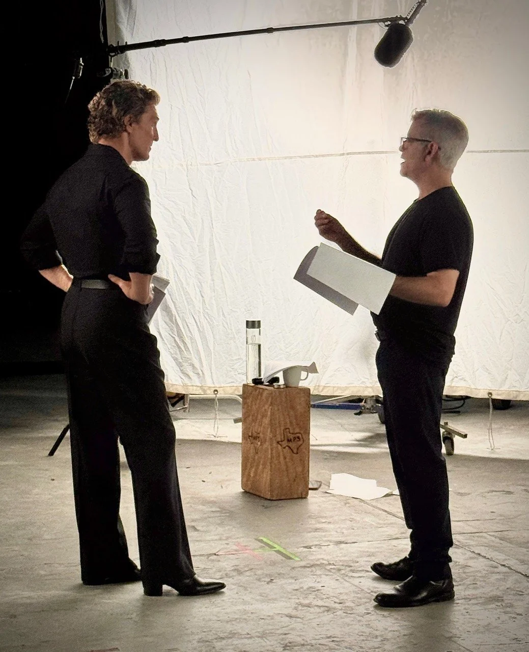 John Zissimos discussing a scene with Matthew McConaughey on set, with scripts and a boom microphone overhead.