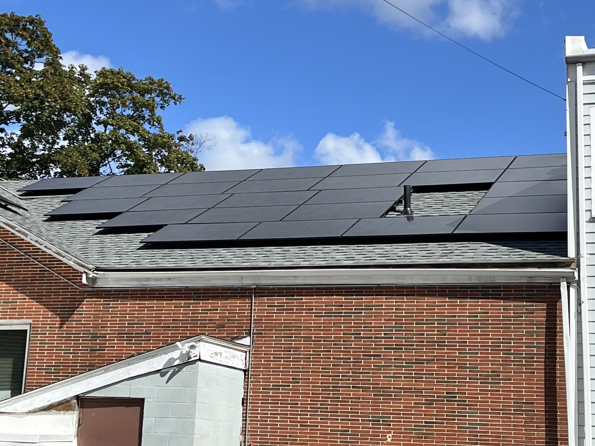 HBT's red-brick building under a bright blue sky, its roof covered with rows of dark solar panels, with tall trees behind.