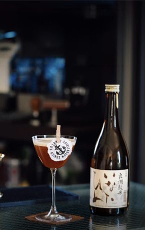 Silent Acid cocktail in a coupe beside a sake bottle