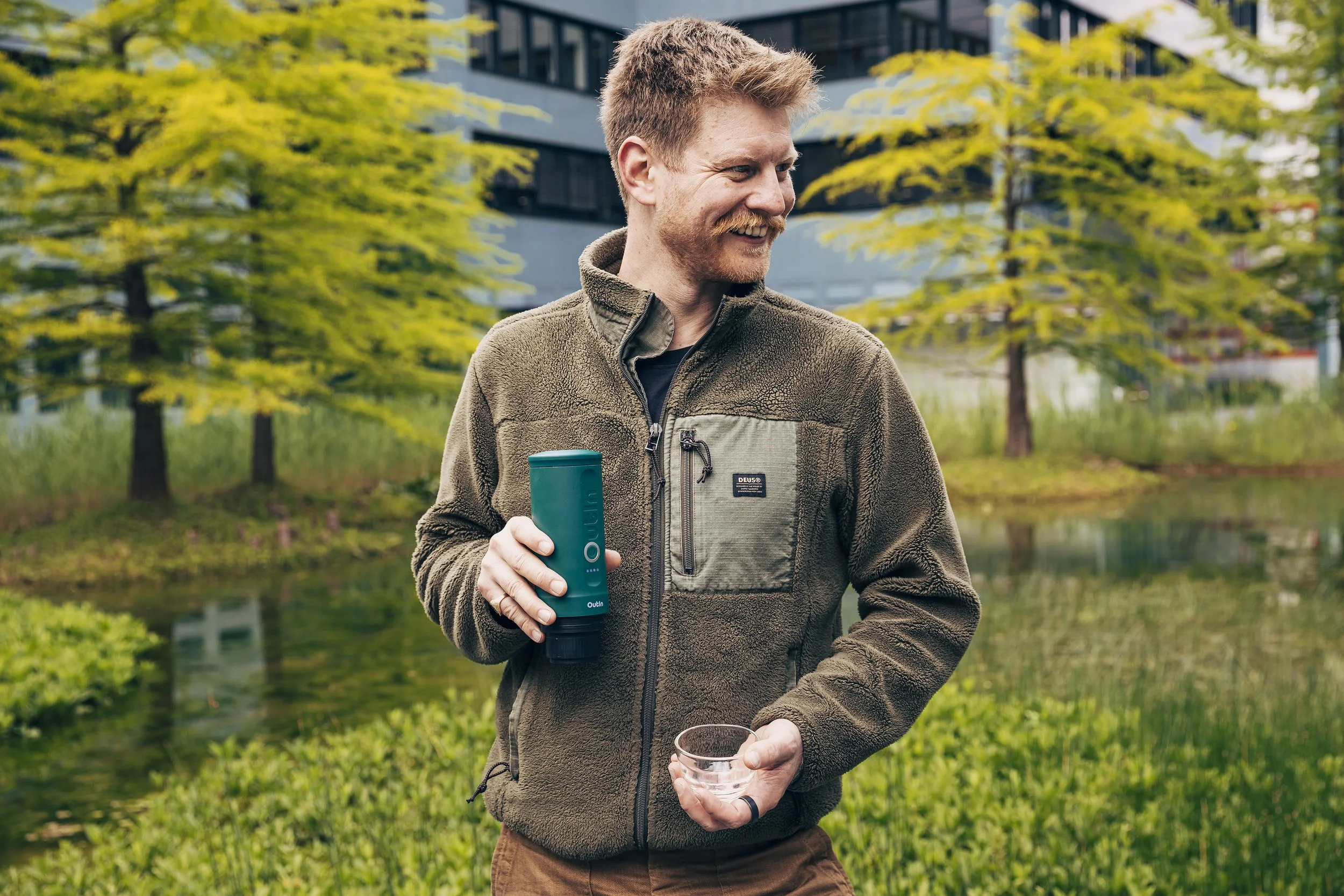Sandro Roth outdoors holding an Outin portable espresso machine and a glass cup