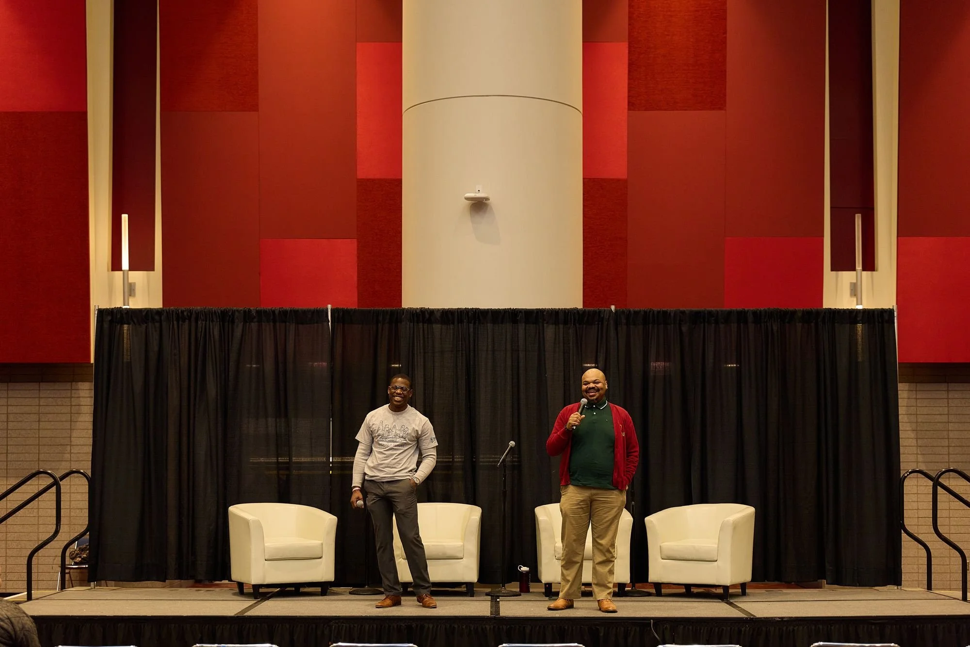 Speakers on stage in front of a red architectural wall
