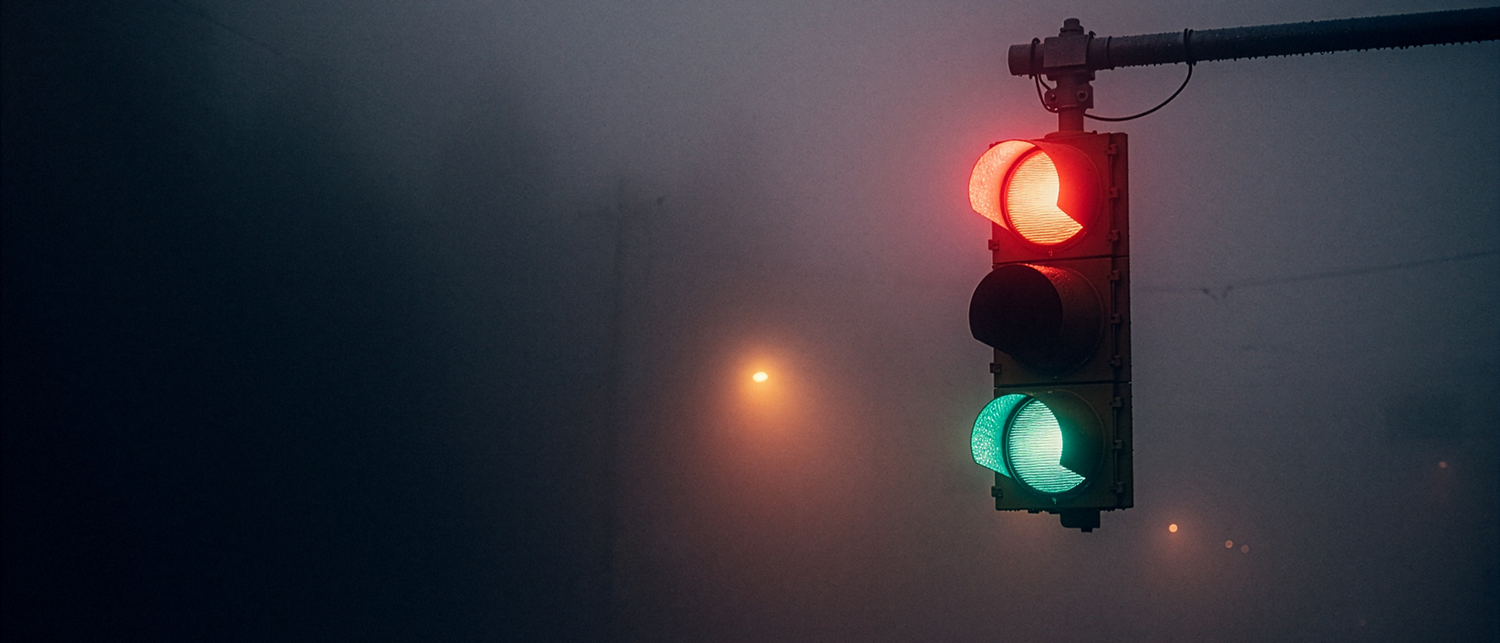 Three signal lamps glowing through fog over an empty wet road
