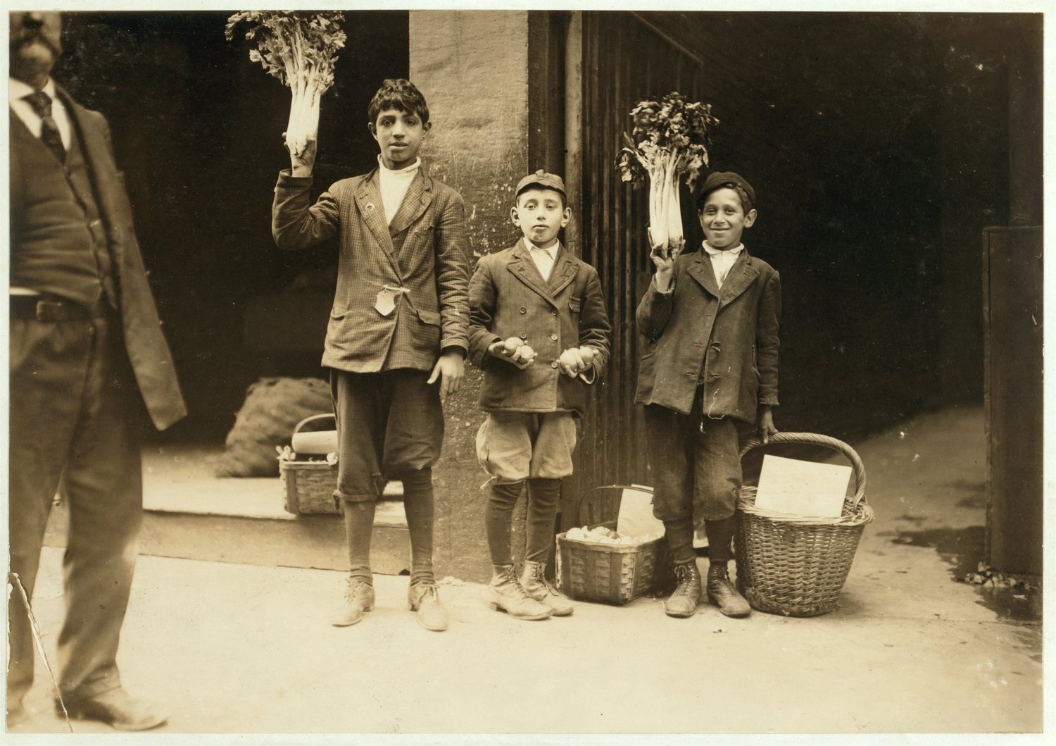 Three boys hold up bunches of celery on a city street