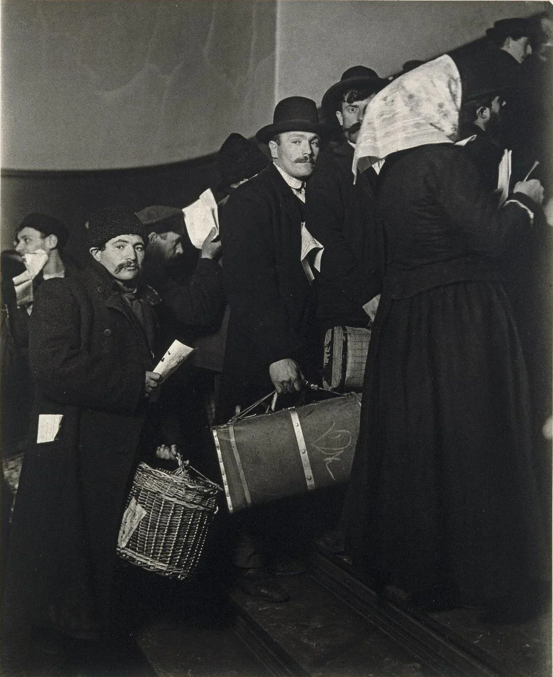Immigrants carrying bundles climb a staircase at Ellis Island
