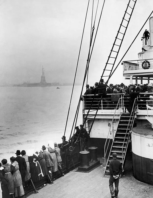 Immigrants on a ship deck see the Statue of Liberty in the distance