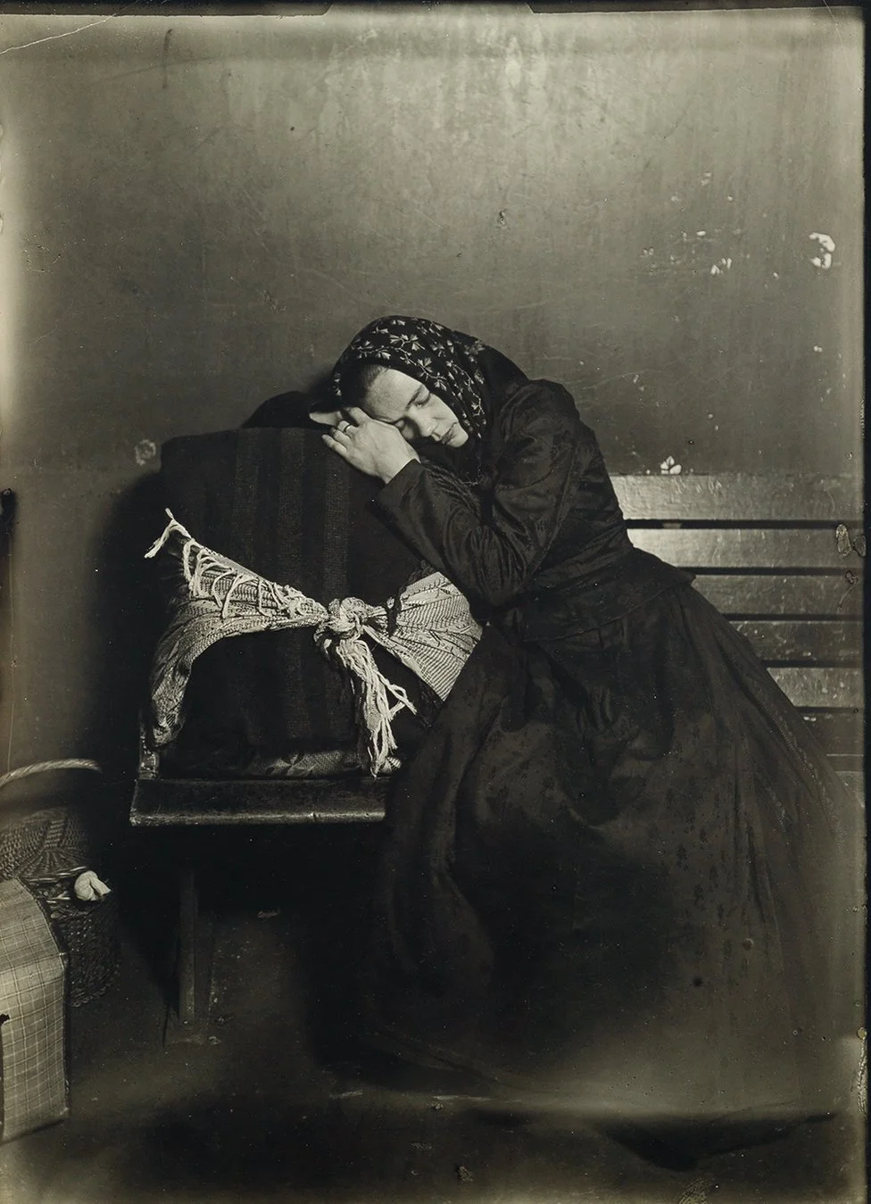 A woman in a headscarf asleep on a bench, her head resting on a tied bundle