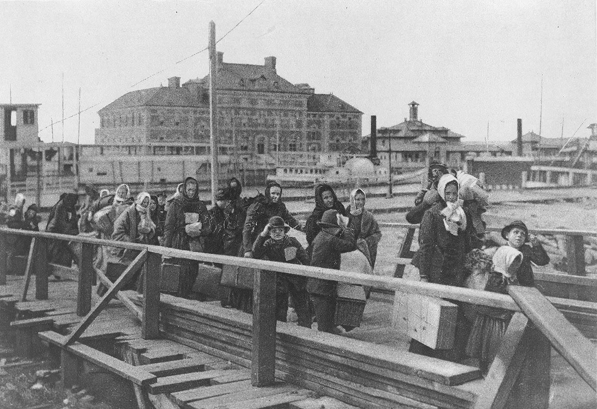 Immigrants walk up a wooden ramp from a barge at Ellis Island