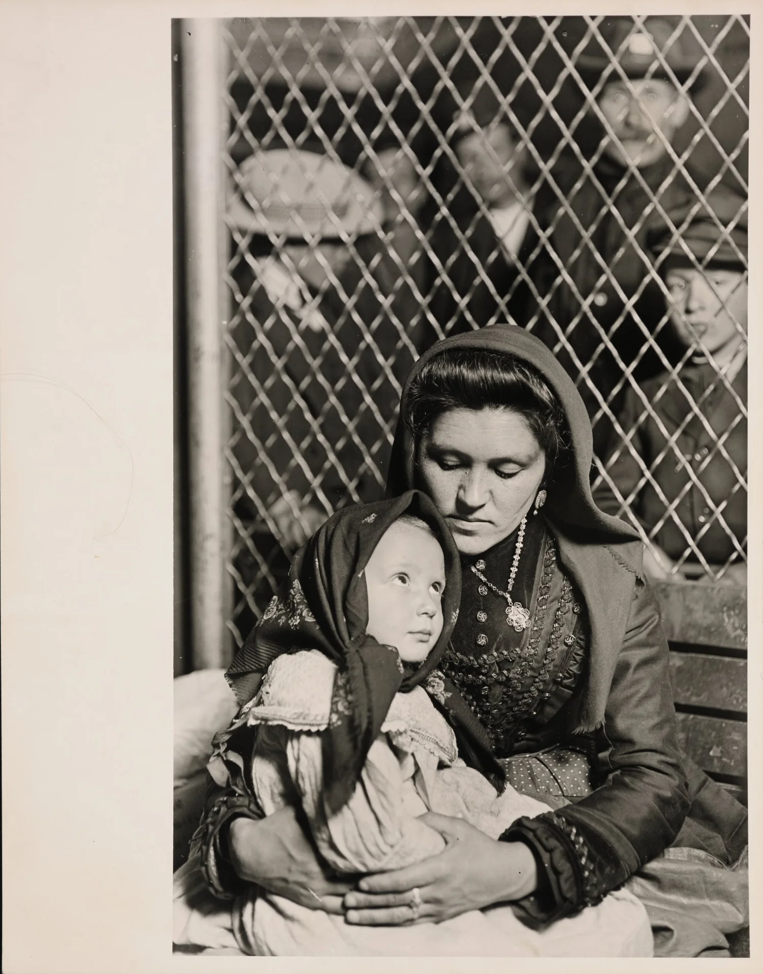 A mother holds her young daughter in front of a wire fence