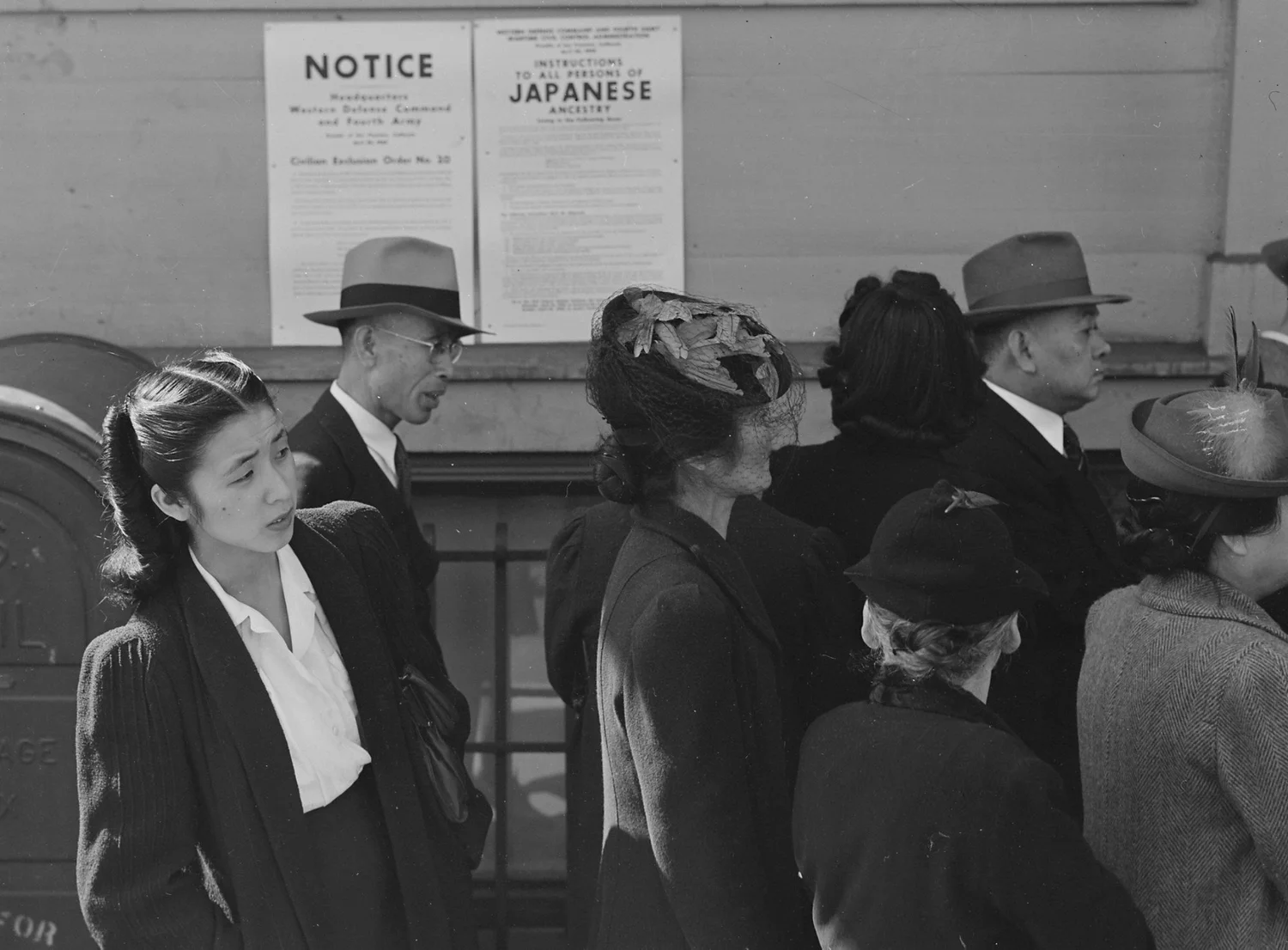 Japanese Americans waiting in line beneath posted exclusion orders