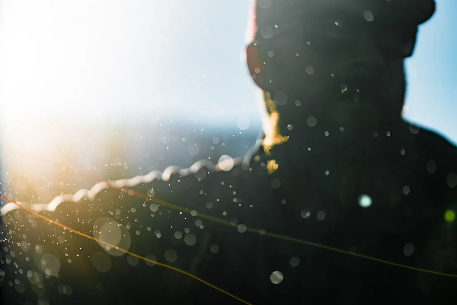 A fly fisherman silhouetted against the sun, spray and line caught in the light