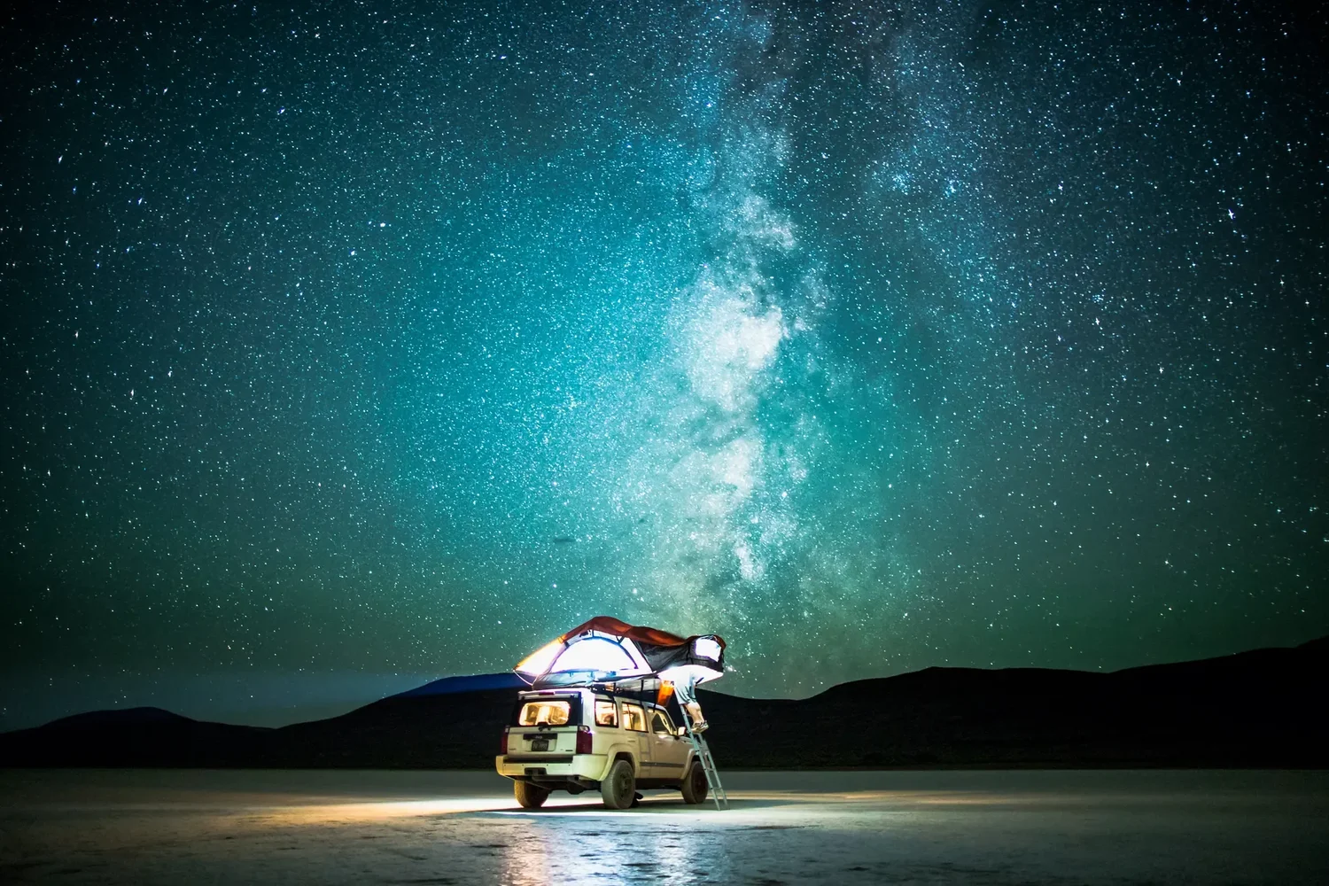 The Milky Way over the Alvord Desert playa with a lit rig below