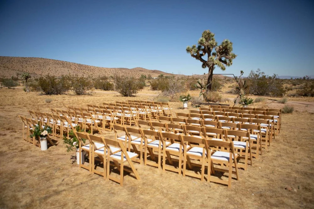 Rows of wooden ceremony chairs set up in the desert at Serenity Escape in Yucca Valley with Joshua trees and blue sky behind them