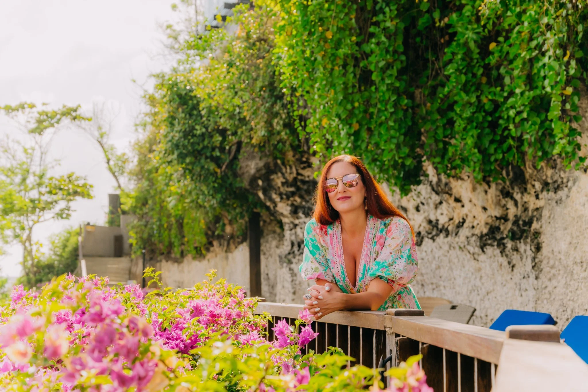 Laura leaning on a terrace railing behind vivid pink flowers in Bali