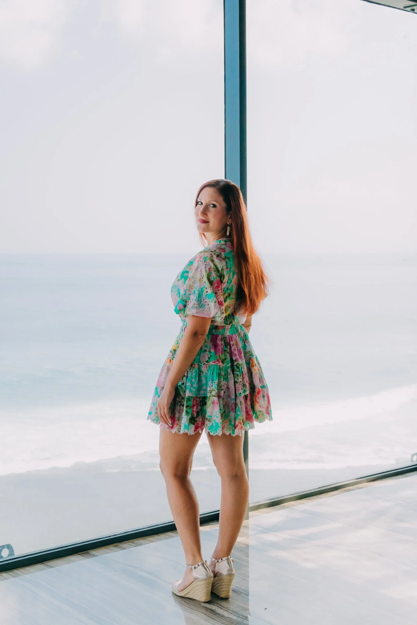 Laura standing beside a glass wall with a bright ocean view in Bali
