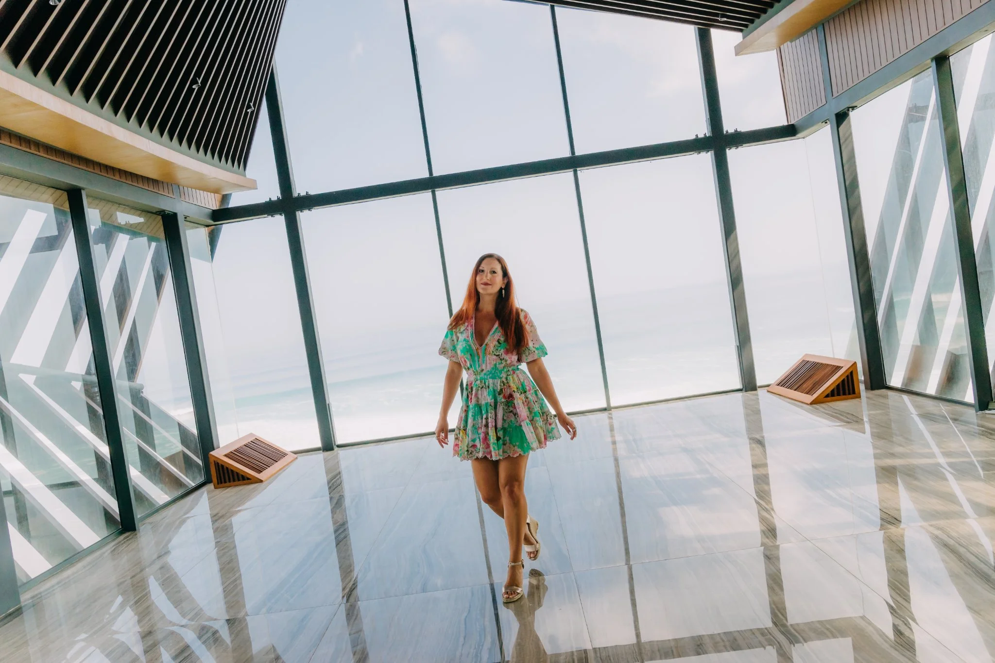 Laura walking through a modern glass pavilion above the ocean in Bali