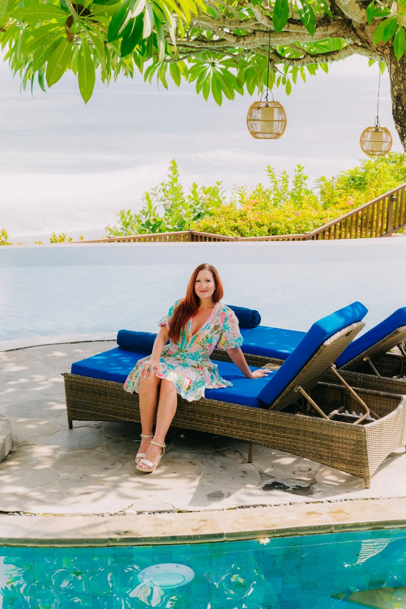 Laura seated on a blue pool lounger with an ocean view in Bali