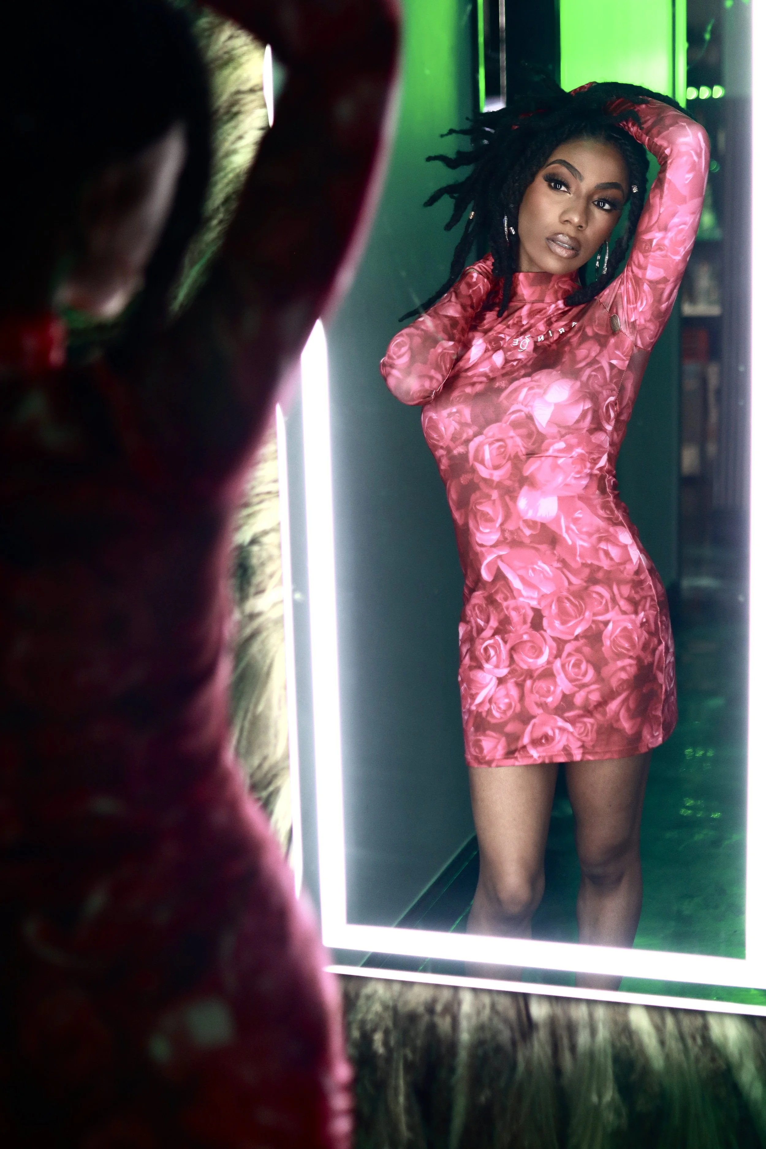Customer posing in a pink floral dress in an illuminated mirror after glam by Dej