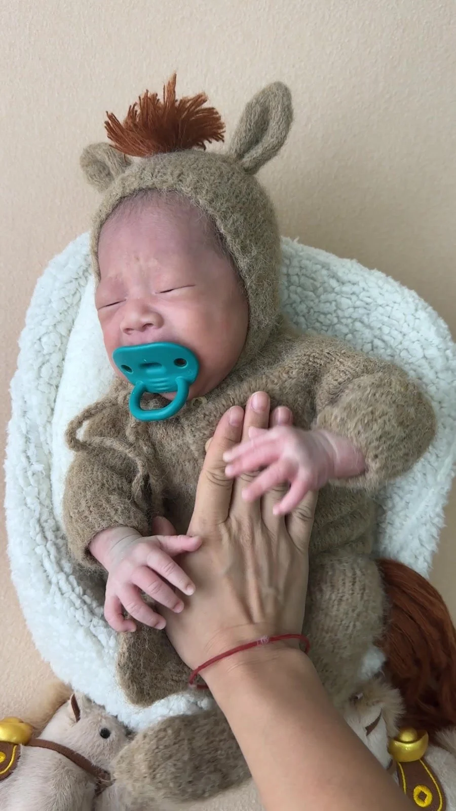 Newborn in a knitted animal outfit showing an unsettled expression before a break during a Mamamiyo home photoshoot in Singapore.