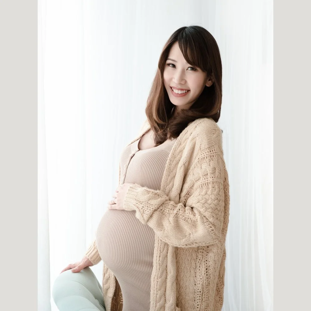 Smiling pregnant woman wearing a beige knitted cardigan over a fitted dress, photographed by Mamamiyo Photography in Singapore