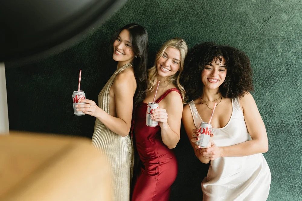 Three friends in evening dresses laughing in front of a green velvet backdrop