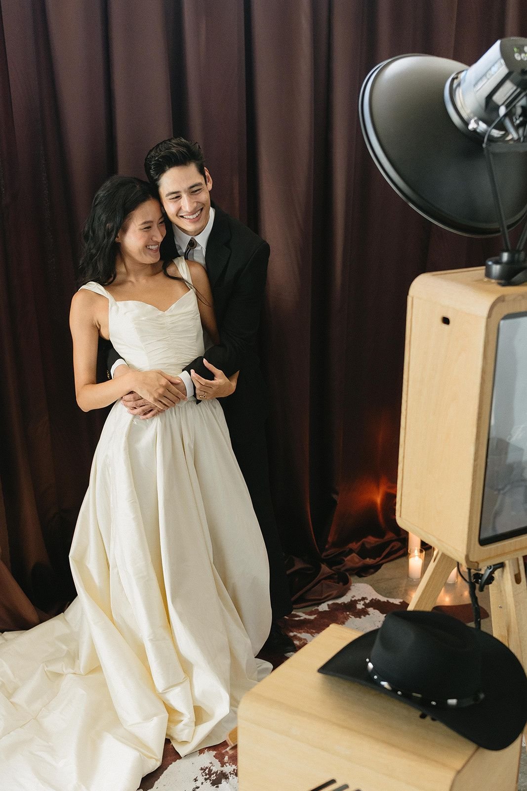 Bride and groom sharing a laugh beside a wooden photo booth at a candlelit wedding reception