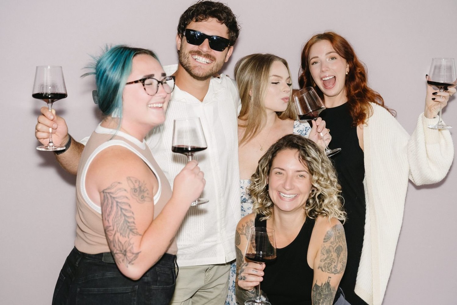 Six friends with wine glasses squeezed into one frame at an open-air photo booth