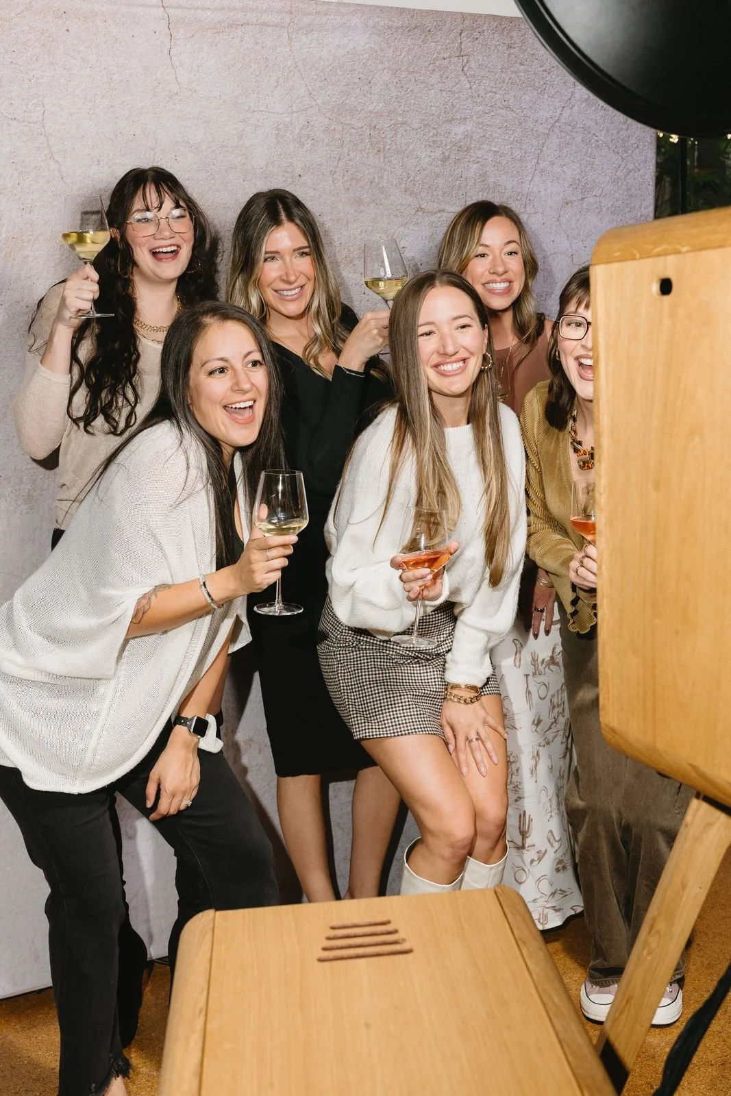 Group of coworkers crowding into one frame at a wooden photo booth during a company party
